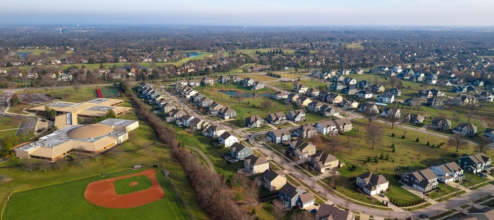 Aerial drone view of a residential suburb in Dublin, Ohio, showing rows of single-family homes, tree-lined streets, a school campus, and a baseball diamond in the foreground.