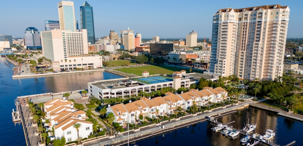 Aerial view of Downtown Jacksonville skyline behind a waterfront townhome community with a marina full of boats
