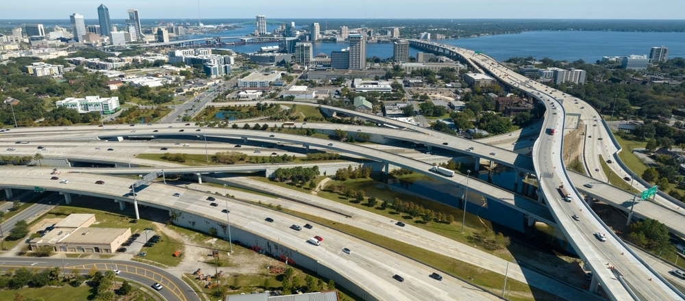 Aerial view of a Jacksonville highway interchange with multiple overpasses leading toward the downtown skyline and river