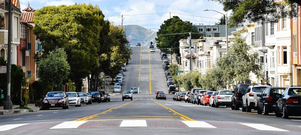 A road over a hill with parked and driving cars in San Francisco